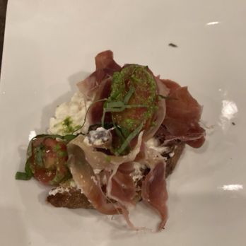 Modern Plate - Burrata toast - prosciutto hard to bite (stringy) - A dish featuring a slice of toast topped with prosciutto, burrata cheese, and green herbs, served on a white plate. - Cocktail Bars Near Me - Elmhurst, Illinois