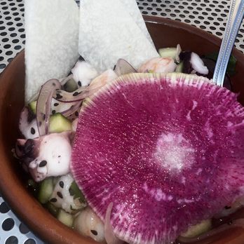 Pilsen Yards - Octopus Ceviche - A bowl of octopus ceviche featuring sliced octopus, cucumber, onion, and a large pink radish slice, garnished with tortilla chips. - Tacos Near Me - Chicago, Illinois