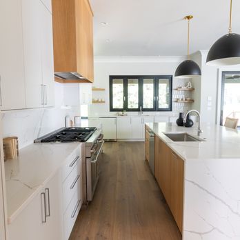 Infinity Custom Cabinets - Bright and airy modern kitchen featuring sleek white cabinetry, with white oak accents, a stainless steel gas range, and a large island. - Cabinetry Near Me - Leland, North Carolina