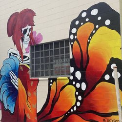 Dragon School murals - Skeleton figure wearing brown wig, sourrounded by green & blue leaves.