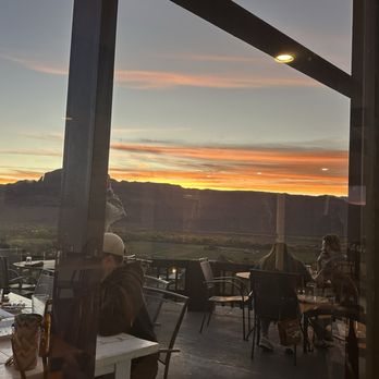 Sunset Grill - Outdoor dining area with several people seated at tables, overlooking a mountain landscape during sunset. - Steakhouses Near Me - Moab, Utah