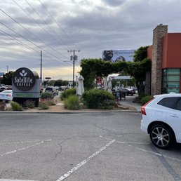 See the sign - Exterior view of Satellite Coffee with a sign, outdoor seating area, and parking lot, located in a commercial area.