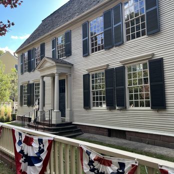 Webb Deane Stevens Museum - A two-story colonial-style house with white siding, black shutters, and a small portico entrance, decorated with patriotic bunting on the fence. - Museums Near Me - Wethersfield, Connecticut