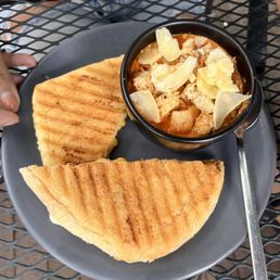 Tomato Soup - A grilled cheese sandwich is served with a bowl of tomato soup topped with cheese shavings on a black plate.