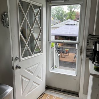 MDR Home Improvement - A door with a diamond-patterned glass panel is open, revealing a window and a view of an outdoor patio with a canopy and seating. - General Contractors Near Me
