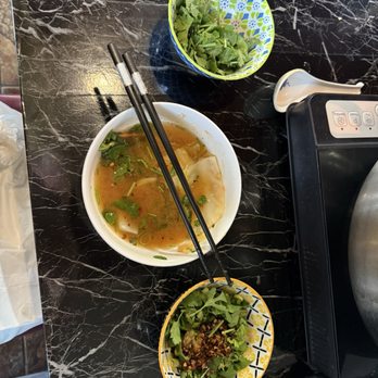 Zu Hot Pot - A hot pot meal with broth and dumplings in a white bowl, accompanied by a salad and a small bowl of greens on a black marble table. - Hot Pot Near Me - Albuquerque, New Mexico