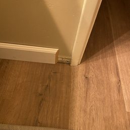 Unfinished bathroom baseboard - The image depicts a corner with a damaged baseboard and a transition between wood and tile flooring.
