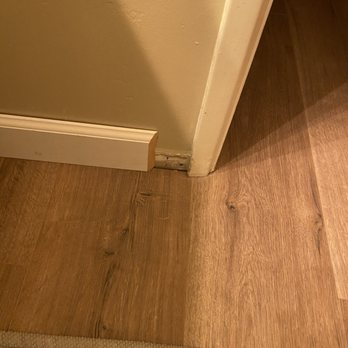 Flooring Direct Temecula - Unfinished bathroom baseboard - The image depicts a corner with a damaged baseboard and a transition between wood and tile flooring. - Carpeting Near Me - Temecula, California
