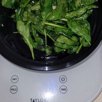 M'tucci's Italian - Sauteed Spinach - The image shows a black bowl containing fresh, green spinach leaves, placed on a digital kitchen scale. The scale displays a weight of 17 grams. The setting appears to be a kitchen countertop with a neutral-colored surface. The spinach leaves are vibrant and appear to be recently washed or prepared for cooking. - Italian Near Me - Albuquerque, New Mexico