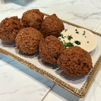 Tabule Restaurant - Falafel ($12.00) - Six falafel balls are arranged on a decorative rectangular plate with a side of white sauce garnished with chopped herbs. - Middle Eastern Near Me - Toronto, Ontario