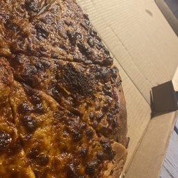 a pizza in a box - The image features a pizza with a dark, crispy crust and cheese topping, partially eaten and placed inside a cardboard pizza box. The pizza appears to have a thick crust with some burnt areas, and the cheese is melted and browned. The box is open, revealing the pizza slices, and the background includes a wooden surface.