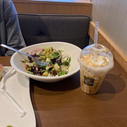 Fuji apple salad and caramel frozen coffee - A salad with mixed greens, onions, and other vegetables is on a white plate, alongside a caramel frozen coffee drink with whipped cream at Panera Bread.