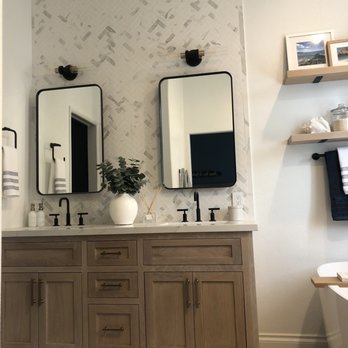 EDW Construction - After - A bathroom features a wooden vanity with two black faucets, two mirrors, and a white vase with greenery on the countertop. - General Contractors Near Me