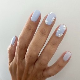What I asked for, they nailed it! Pun intended! - A close-up image of a hand with nails painted in a pastel blue color. Several nails are decorated with white daisy flower designs, creating a floral nail art pattern. The background is plain and light-colored, emphasizing the nails and their detailed design.