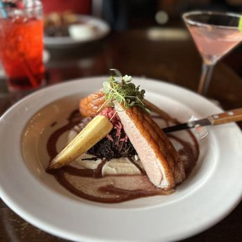 Johnny Seesaw's - Duck Entree (very small portion)  Should be labeled as an appetizer - A plated entrée featuring a slice of cooked meat, vegetables, and sauce, garnished with microgreens, served on a white plate at a restaurant. - American Near Me - Peru, Vermont
