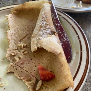 Poppycock's - Bad wrap - A partially eaten crepe with powdered sugar and a small piece of tomato on a plate. The crepe appears thin and slightly crispy, with some crumbs and remnants of filling. The plate has a brown and white rim, and there are other plates and utensils visible in the background, indicating a meal setting. - Breakfast & Brunch Near Me - Aspen, Colorado