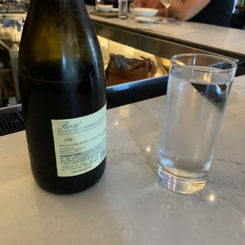 The Eastern - Lambrusco, a full sparkling rosé - A bottle of Reggiano Rosé sparkling wine and a glass of water are placed on a bar counter in a restaurant setting. - Wine Bars Near Me - Washington, DC, District of Columbia