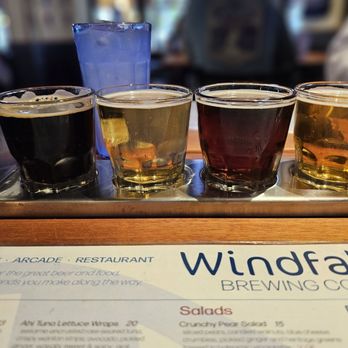 Windfall Brewing - Birthday dinner flight? - Four small glasses of beer with varying colors are arranged on a metal tray at Windfall Brewing Co., with a menu visible in the foreground. - Steakhouses Near Me - Westminster, Colorado