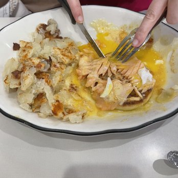 Peppercorn - Lox Benedict - A person is holding a knife and fork, cutting into a cooked salmon fillet on a white, oval-shaped dish. The dish also contains mashed potatoes with a browned top. The person is wearing a red shirt, and the image is taken from above, showing the food and utensils clearly. - Diners Near Me - Summit, New Jersey