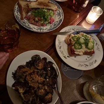 Swoony's - Dinner - The image shows a dining table with a sandwich, a pasta dish, and a slice of pizza topped with jalapeños, along with drinks and candles. - New American Near Me - Brooklyn, New York