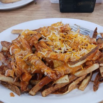 Lupton Truck Stop - Chili cheese fries. - A white plate holds chili cheese fries with shredded cheese on top, served on a wooden table at a restaurant. - Service Stations Near Me - Lupton, Arizona