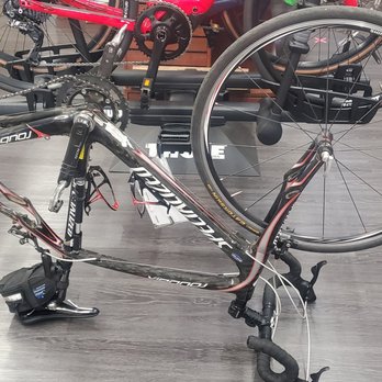 Ray's Cycle - A road bike is positioned upside down on a repair stand in a bike shop, with water bottles nearby and other bikes in the background. - Bikes Near Me - Vacaville, California