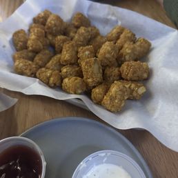 Over cooked crap - Fried chicken nuggets are served in a basket lined with paper, accompanied by dipping sauces on a wooden table.