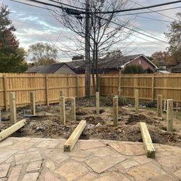 Deck Construction - Wooden posts are being installed for a new deck in a backyard, with a stone patio in the foreground and a wooden fence in the background.