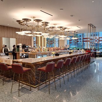 Solette - A spacious bar area with a marble counter, red upholstered chairs, and contemporary lighting fixtures in a restaurant setting. - American Near Me - Chicago, Illinois