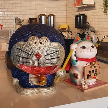 Uni BUBBLE TEA - a kitchen counter with a counter top - Statues of Doraemon and a Maneki-neko are displayed on a cafe counter, with a white tiled wall and coffee equipment in the background. - Bubble Tea Near Me - Bradford, Ontario