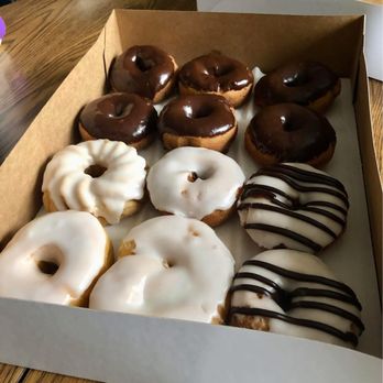 Allegretti's Bakery - A box contains nine donuts with various icings: six chocolate-glazed, three with white icing, and two with white icing and dark drizzle, on a wooden table. - Bakeries Near Me - Norridge, Illinois