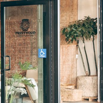 Apostrophe Home - A glass storefront door with an accessible sign leads into a space decorated with plants and vintage rugs, suggesting a home decor or furniture store. - Home Decor Near Me - Encinitas, California