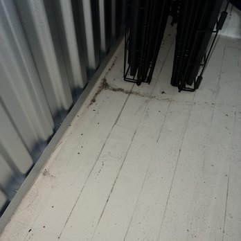 Go Store It Self Storage - Dust and dirt are accumulated along the base of a metal wall and on the white floor, near black metal racks. - Self Storage Near Me - Cincinnati, Ohio