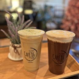 Jasmine Green Tea - Two iced beverages from Café 86, one with a light color and the other darker, are placed on a wooden tray with a potted plant behind them.