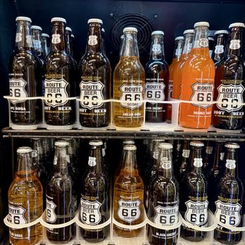 Covered Wagon - The image shows a vending machine stocked with bottles of Route 66-themed beverages, including soda and beer. The bottles are arranged on multiple shelves, with labels displaying flavors such as cream soda, orange soda, and root beer. The bottles are made of glass, with some having white caps and others with metal caps. The top of the vending machine features a strip of LED lighting, illuminating the bottles. The background includes a ventilation fan and a dark interior of the vending machine. - Jewelry Near Me - Albuquerque, New Mexico