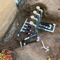 PVC pipes and valves are installed in a trench at a construction site, likely for irrigation or plumbing system setup.