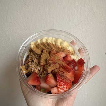 Better Blend - Super Bowl - A transparent bowl contains sliced strawberries, banana slices, granola, and cinnamon, held by a person's hand against a plain wall. - Juice Bars & Smoothies Near Me - Cincinnati, Ohio