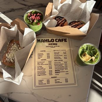 Kahlo Cafe - Chocolate Chip cookie and Brownie - A marble table holds two green drinks with toppings, two boxes of donuts, and a sandwich, with a Kahlo Cafe menu in the center. - Bakeries Near Me - Oceanside, California