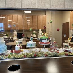 Cake cake cake - A variety of decorated cakes and Christmas ornaments are arranged on a table behind a glass window, with holiday decorations and a reflection of the room.