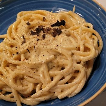 Cafe Bionda - A bowl of creamy pasta, likely fettuccine or linguine, is presented in a blue ceramic dish. The pasta is coated in a white sauce and garnished with thin black truffle shavings and black pepper. The setting suggests a dining environment, possibly at an Italian restaurant known for pasta dishes. - Italian Near Me - Chicago, Illinois