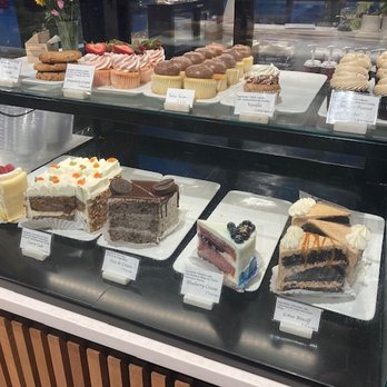 Cake Bar - The display in the Salt City Market - A glass display case showcases an assortment of cakes and cupcakes, including layered, frosted, and decorated varieties, in a bakery or dessert shop setting. - Food Stands Near Me - Syracuse, New York