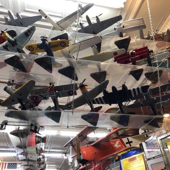 Dick's 5 & 10 - Collection of model airplanes - Multiple model airplanes are hanging from the ceiling of a store, arranged in a layered display. The models vary in size, color, and design, representing different types of aircraft such as military planes, commercial jets, and vintage models. The store interior includes ceiling details and lighting, with some framed items and signage visible at the bottom of the image. - Discount Store Near Me - Branson, Missouri