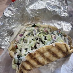 Lamb Gyro - A gyro with chopped vegetables and sauce, wrapped in grilled flatbread, partially covered with aluminum foil.