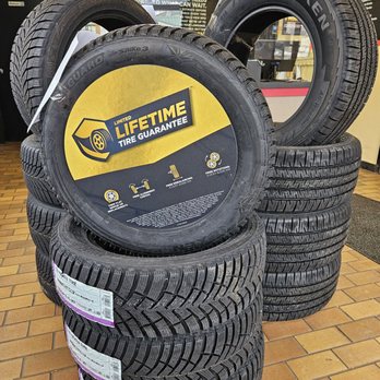 Midas - Multiple stacks of tires are displayed inside a tire shop, including a promotional tire with a lifetime guarantee sign. - Auto Repair Near Me - Markham, Ontario