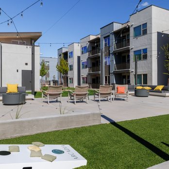 Arcadia - Outdoor lounge with seating, string lights, and cornhole game area surrounded by modern apartment buildings and landscaped greenery. - Apartments Near Me - Santa Fe, New Mexico