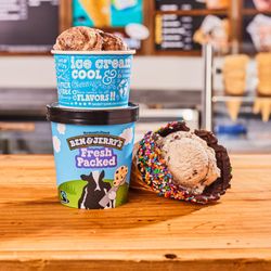 Ben & Jerry’s - Waffle cone, cup and fresh packed pint in front of Ben & Jerry's ice cream shop menu board.