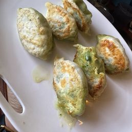 Pan Fried Chicken Dumplings - Six pan-fried pork dumplings with crispy edges are arranged on a white plate, some with green onion bits and a small amount of oil.