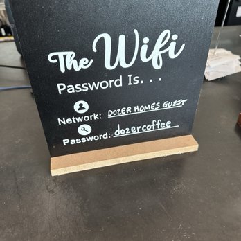 DOZER Coffee - Wifi - The image shows a blackboard-style sign with white handwritten text placed on a countertop at Dozer Coffee. It displays Wi-Fi information, including the network name 'DOZER HOMES GUEST' and the password 'dozercoffee'. The sign is supported by a wooden base and is situated in a coffee shop environment, with kitchen and counter items visible in the background. - Cafes Near Me - Ann Arbor, Michigan