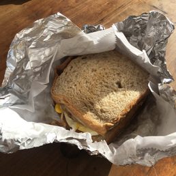 Breakfast Sandwich - A breakfast sandwich with egg, cheese, and possibly bacon or sausage, wrapped in aluminum foil, on a wooden table.