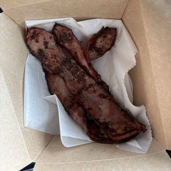 Bread and Butter Kitchen - Turkey bacon - A strip of cooked bacon with grill marks is placed inside a cardboard takeout box lined with parchment paper. - Breakfast & Brunch Near Me - Annapolis, Maryland